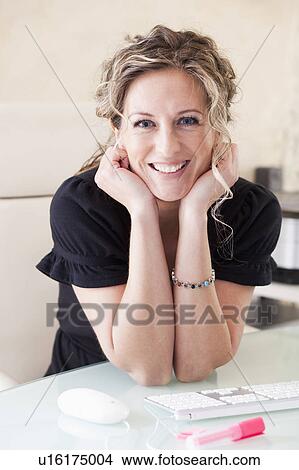 Picture - Woman sitting at her desk smiling. Fotosearch