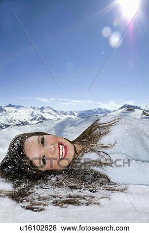 Stock Photo - Woman smiles laying in snow. Fotosearch