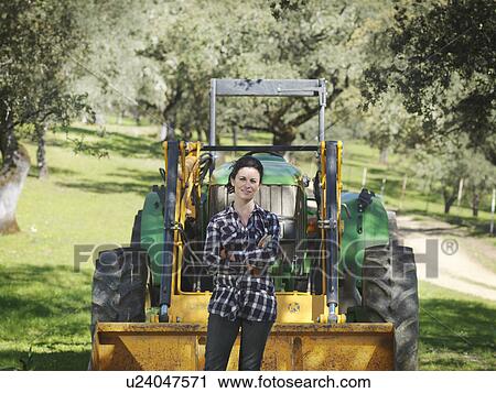 Stock Image - Woman standing in front of tractor. Fotosearch