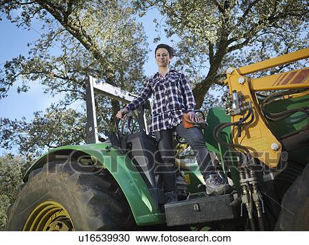 Stock Image - Woman standing on tractor. Fotosearch