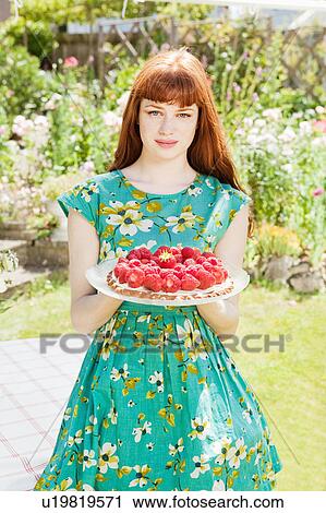 Stock Image - woman stands strawberry tart in garden. . Fotosearch