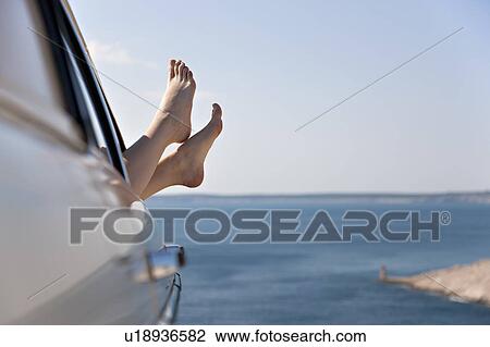 Stock Image - Woman stretching feet from car by sea. Fotosearch