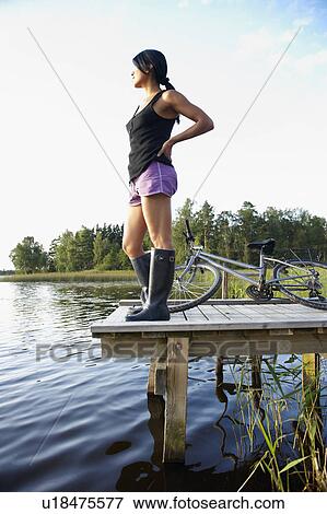 Stock Photo - Woman with bike, at the end of a dock. Fotosearch