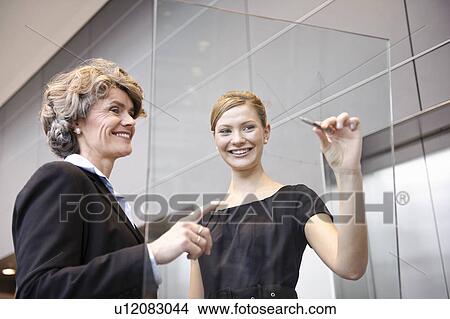 Picture - Young businesswomen writing on glass. Fotosearch