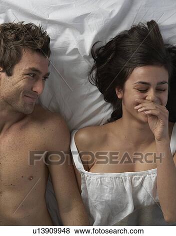 Stock Photo - Young couple in bed laughing, high angle. Fotosearch