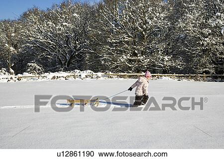 Stock Image - Young girl pulling sledge in snow. Fotosearch