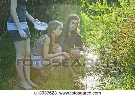 Stock Image - Young man and women catching tadpoles. Fotosearch