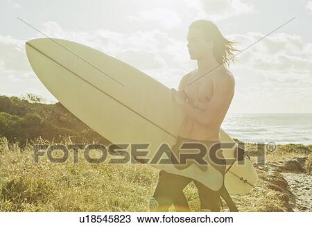 Stock Image - Young man holding surfboard. Fotosearch