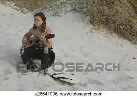 Stock Photograph - Young man playing guitar on beach. Fotosearch