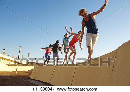 Young people balancing on wall View Large Photo Image Stock Photo - Young people balancing on wall. Fotosearch