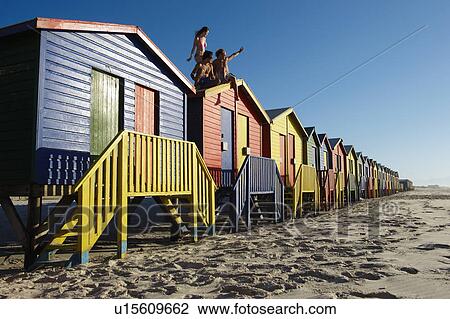 Stock Image - Young people sitting on top of beach hut. Fotosearch