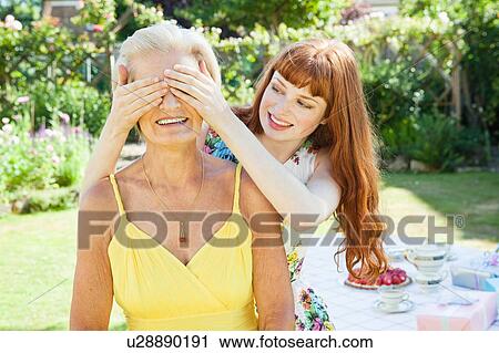 Stock Image - young woman covers eyes of mature woman.. Fotosearch