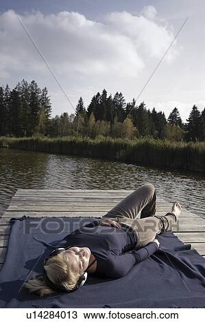 Stock Image - Young woman lies on blanket on jetty. Fotosearch