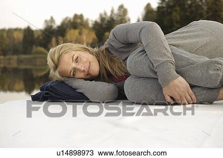 Stock Image - Young woman lying on blanket by lake. Fotosearch