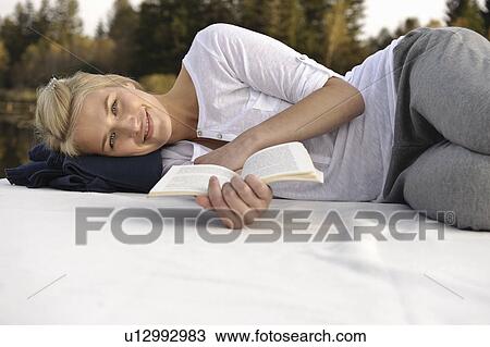 Stock Image - Young woman lying on blanket, reading. Fotosearch