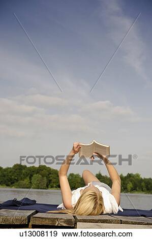 Stock Photo - Young woman lying on blanket, reading. Fotosearch