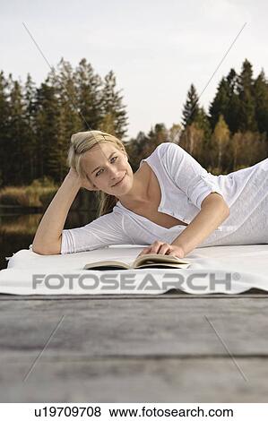 Stock Photo - Young woman lying on blanket, reading. Fotosearch