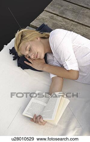 Stock Photo - Young woman lying on blanket, reading. Fotosearch
