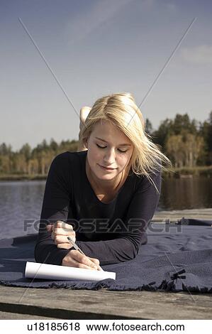 Stock Photo - Young woman lying on blanket, writing. Fotosearch