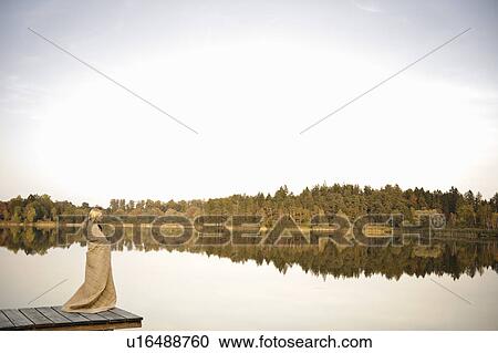 Stock Image - Young woman standing on jetty, enjoying. Fotosearch