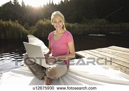 Stock Image - Young woman using laptop, smiling. Fotosearch