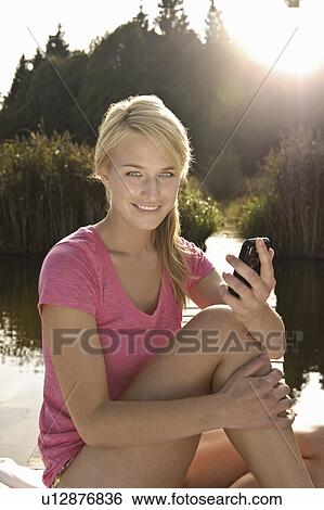 Stock Photograph - Young woman using mobile phone, smiling. Fotosearch
