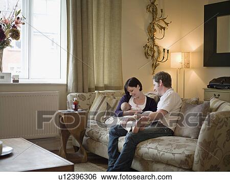 Stock Photograph - A couple and new baby sitting on a sofa. Fotosearch