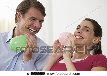 Stock Photo - a couple having fun blowing balloons. Fotosearch