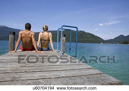 A couple sitting on a pier by a lake View Large Photo Image Picture - A couple sitting on a pier by a lake. Fotosearch