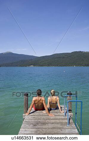 Stock Image - A couple sitting on a pier by a lake. Fotosearch