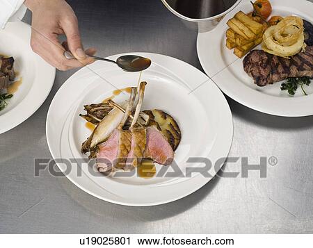 Stock Image - A hand drizzling gravy on some lamb. Fotosearch