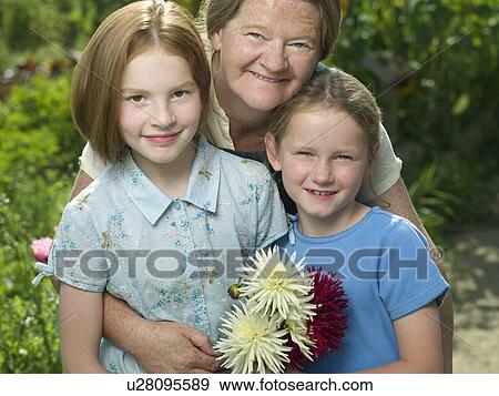 Stock Photo - A woman hugging two girls in a garden. Fotosearch