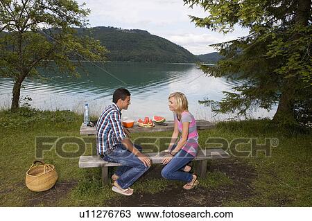 Stock Image - A young couple having a picnic by a lake. Fotosearch