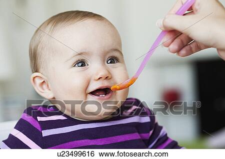 Stock Photograph - baby sitting in chair being fed. Fotosearch