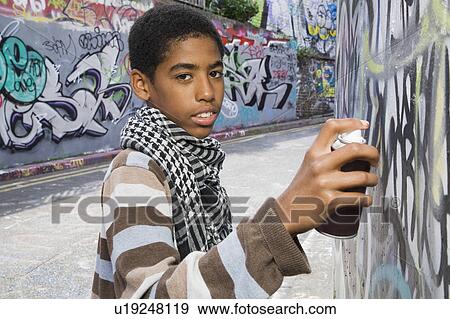 Stock Photo - Black Teenager doing graffiti on a wall. Fotosearch