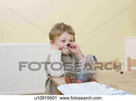 Stock Image - boy holding berry on nose. Fotosearch