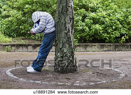 Boy leaning on tree with ball View Large Photo Image Picture - Boy leaning on tree with ball. Fotosearch