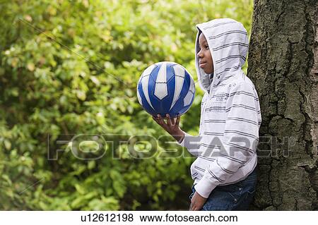 Boy leaning on tree with ball View Large Photo Image Stock Photo - Boy leaning on tree with ball. Fotosearch