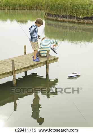 Stock Photography - Boys playing with toy boat on jetty. Fotosearch