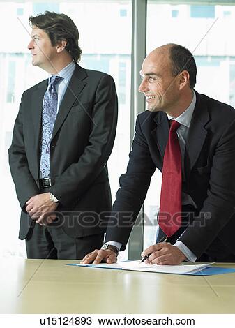 Stock Image - Business man signing papers with partner. Fotosearch