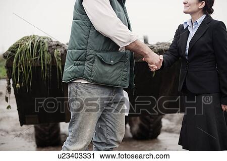 Stock Image - business woman shaking hands with farmer. Fotosearch