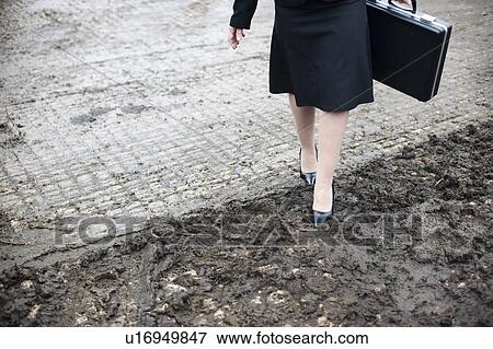 Stock Photo - business woman walking in muddy farm. Fotosearch
