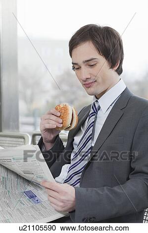 Stock Image - businessman reading whilst eating. Fotosearch