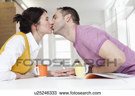 Stock Image - couple leaning over table kissing. Fotosearch