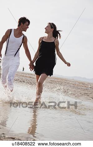 Stock Image - couple running along the beach. Fotosearch