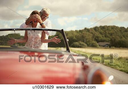 Stock Photo - Couple with car, his hands over his eyes. Fotosearch