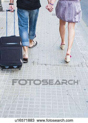 Stock Image - couple with trolly walking along street. Fotosearch