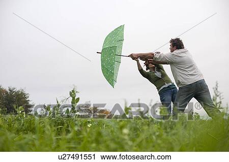 Stock Image - couple with umbrella in windy field. Fotosearch