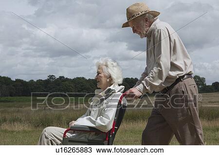 Stock Image - Elderly man pushing woman in wheelchair. Fotosearch