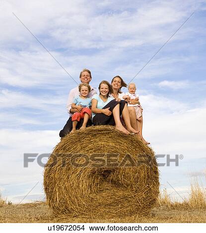 Picture - family of five sitting on hay bale. Fotosearch